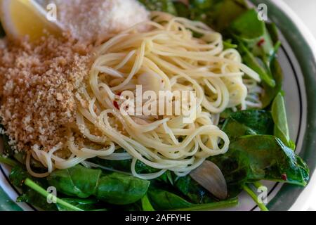 Close-up su capellini angel hair pasta con olio di oliva vergine, spinaci freschi limone, peperoncino fiocchi, aglio e pane tostato briciole, cena angolo di visione Foto Stock