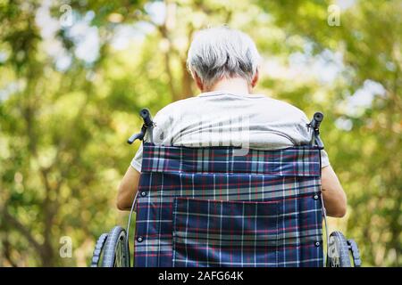 Vista posteriore di asian vecchio seduto all'esterno in sedia a rotelle, a testa in giù Foto Stock