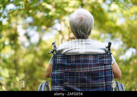 Vista posteriore di asian senior uomo seduto all'aperto nella sedia a rotelle cercando il gemito Foto Stock