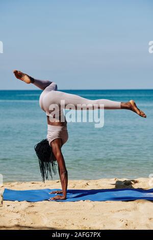 Slim giovane Nero donna che lavora fuori dall'oceano e praticare handstand Foto Stock