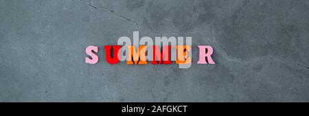 Il variopinto estate parola è fatta di lettere in legno su un grigio muro intonacato sfondo Foto Stock