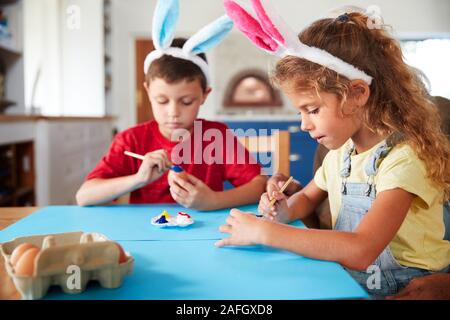 Bambini indossare orecchie di coniglio decorare le uova di Pasqua in casa insieme Foto Stock