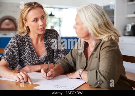 Amico femminile aiutando donna Senior per completare l'ultima volontà e testamento a casa Foto Stock