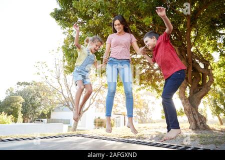 Fratelli con la sorella adolescente giocando sul trampolino all'aperto in giardino Foto Stock