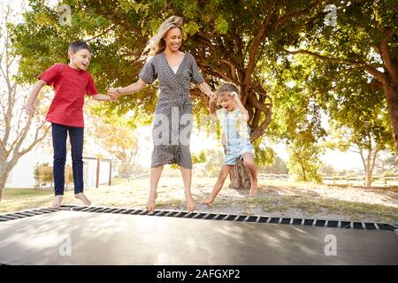 La madre a giocare con i bambini sul trampolino all'aperto in giardino Foto Stock