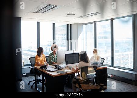 Quattro femmine colleghi creativi che lavorano insieme in un ufficio, visto attraverso la parete in vetro Foto Stock