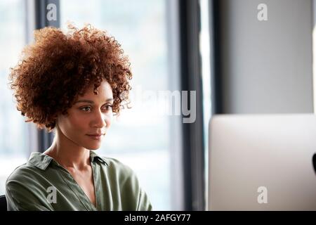 Giovane femmina nero creative seduti ad una scrivania guardando il monitor di un computer, chiudere fino Foto Stock
