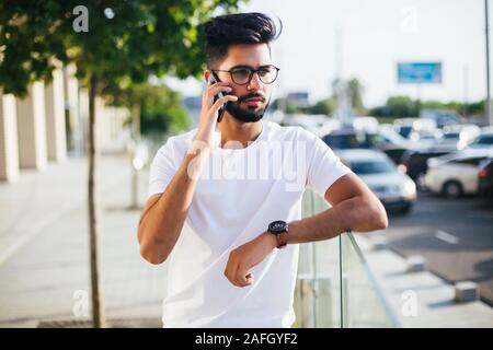 Uomo bello chiamata con il cellulare sorriso outdoor city street, giovane imprenditore attraente casual maglietta blu parlando Foto Stock