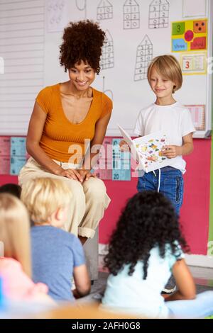 Pupilla d maschio nella scuola elementare di lettura in Aula Libro di classe con docente Foto Stock