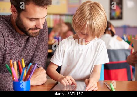 Insegnante di scuola elementare e pupilla maschio disegno usando digitale compressa in aula Foto Stock