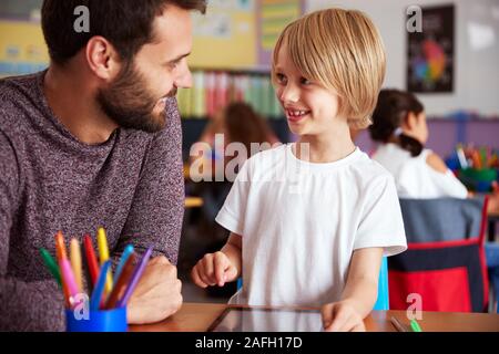 Insegnante di scuola elementare e pupilla maschio disegno usando digitale compressa in aula Foto Stock