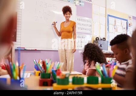 Insegnante femminile in piedi alla lavagna insegnamento lezione di matematica per gli studenti elementari in aula scolastica Foto Stock