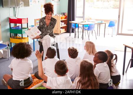 Pupilla elementari che indossano uniformi di alza la mano per rispondere alla domanda come insegnante femminile legge prenota Foto Stock