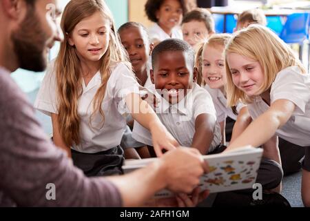 Insegnante maschio alla lettura della storia di un gruppo di alunni elementari che indossano uniformi in aula scolastica Foto Stock
