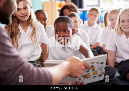 Insegnante maschio alla lettura della storia di un gruppo di alunni elementari che indossano uniformi in aula scolastica Foto Stock