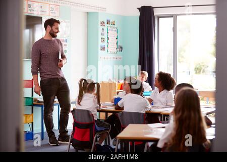 Insegnante maschio Azienda digitale compressa insegna Gruppo di uniformata elementari di alunni in aula scolastica Foto Stock