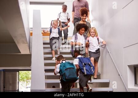Insegnanti e alunni a piedi giù per le scale nella trafficata e Scuola Elementare corridoio Foto Stock