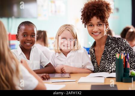 Ritratto di donna con insegnante di scuola elementare gli alunni indossano uniformi utilizzando tavoletta digitale Foto Stock