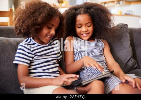 Fratello e Sorella seduti sul divano di casa a giocare con tavoletta digitale Foto Stock