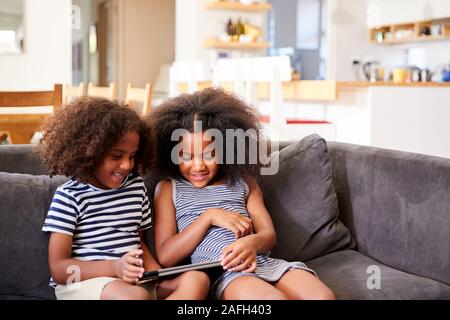 Fratello e Sorella seduti sul divano di casa a giocare con tavoletta digitale Foto Stock