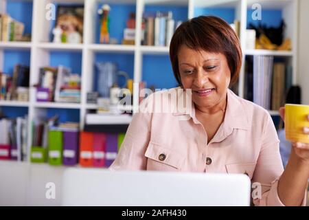 Sorridente donna matura con computer portatili che lavorano in ufficio in casa Foto Stock