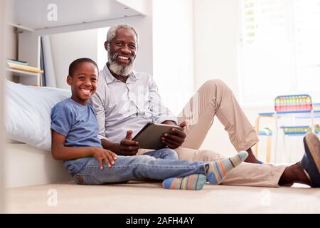 Ritratto di Nonno seduto con il nipote In camera da letto per i bambini con tavoletta digitale insieme Foto Stock