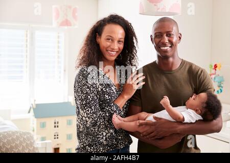 Ritratto di amare i genitori in piedi in vivaio Cuddling figlio Bambino a casa Foto Stock