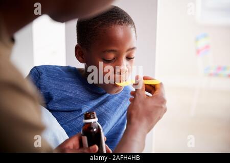 Padre dando figlio malato a letto malato medicina da bottiglia Foto Stock