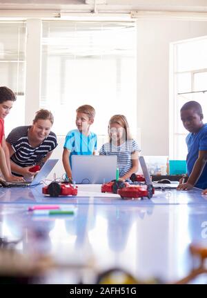 Gruppo di studenti nella scuola dopo la codifica del calcolatore classe imparare a programmare un veicolo robot Foto Stock