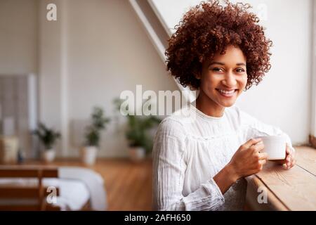 Ritratto di giovane donna in Relax Appartamento Loft guardando fuori della finestra con bevanda calda Foto Stock