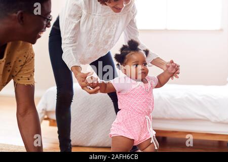 I genitori a casa incoraggiando la nostra bambina di prendere i primi passi Foto Stock