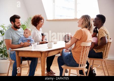 Due famiglie con bebè incontro e conversazione attorno al tavolo sulla data di gioco a casa Foto Stock