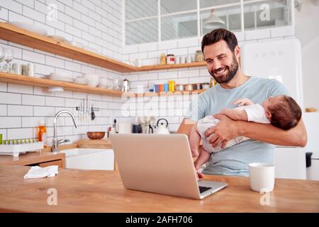 Multitasking Padre tiene il bambino dorme figlio e funziona su computer portatile in cucina Foto Stock