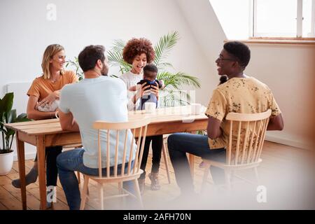 Due famiglie con bebè incontro e conversazione attorno al tavolo sulla data di gioco a casa Foto Stock