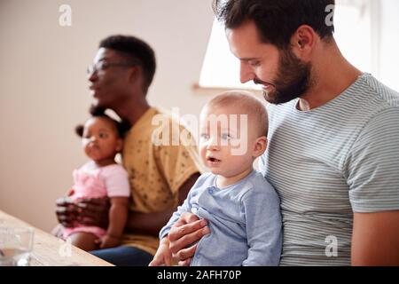 Due famiglie con bebè incontro e conversazione attorno al tavolo sulla data di Gioco Foto Stock