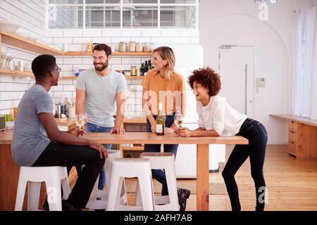 Due coppie relax In cucina a casa con un bicchiere di vino a parlare insieme Foto Stock