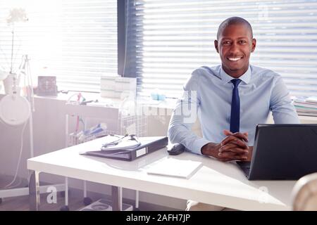 Ritratto di sorridente medico maschile seduto alla scrivania in ufficio Foto Stock