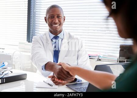 Paziente di sesso femminile si stringono la mano con il medico seduto alla scrivania in ufficio Foto Stock