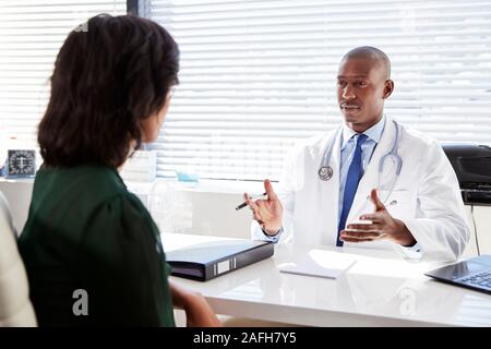 Paziente di sesso femminile in consultazione con il medico seduto alla scrivania in ufficio Foto Stock