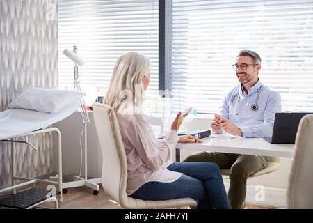 Femmina matura paziente in consultazione con il medico seduto alla scrivania in ufficio Foto Stock