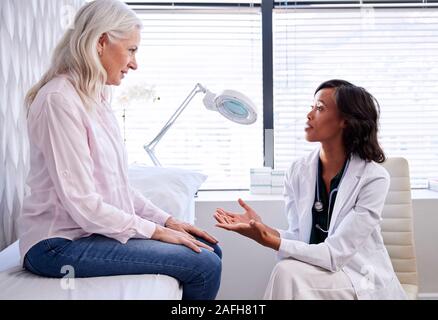 Donna matura in consultazione con il medico donna seduta sul lettino da visita in ufficio Foto Stock