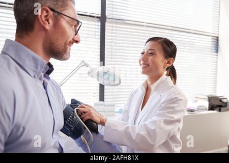 Paziente di sesso maschile avente la pressione del sangue presa dal medico donna in Office Foto Stock