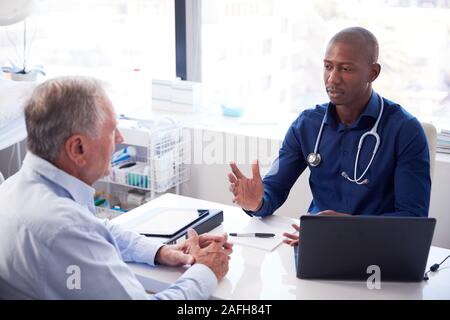 Senior paziente di sesso maschile in consultazione con il medico seduto alla scrivania in ufficio Foto Stock