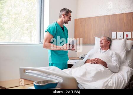 Chirurgo con tavoletta digitale visitando Senior paziente di sesso maschile nel letto di ospedale in unità Geriatrica Foto Stock