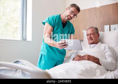 Chirurgo con tavoletta digitale visitando Senior paziente di sesso maschile nel letto di ospedale in unità Geriatrica Foto Stock