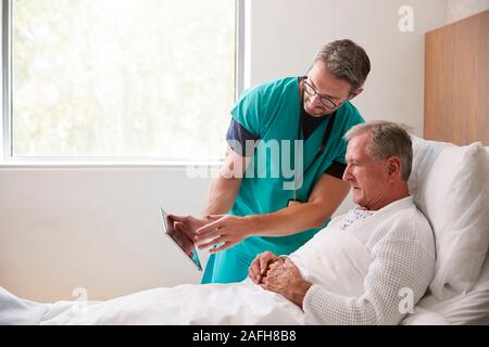 Chirurgo con tavoletta digitale visitando Senior paziente di sesso maschile nel letto di ospedale in unità Geriatrica Foto Stock