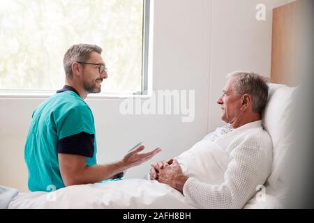 Chirurgo visitando e parlando con i Senior paziente di sesso maschile nel letto di ospedale in unità Geriatrica Foto Stock