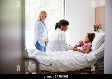 Medico donna in visita a madre e figlia che giace nel letto di ospedale Foto Stock