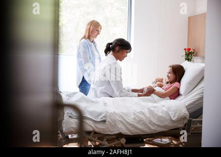 Medico donna in visita a madre e figlia che giace nel letto di ospedale Foto Stock