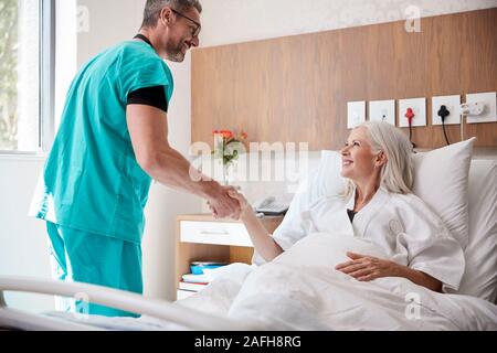 Chirurgo visitando e stringono le mani con femmina matura paziente nel letto di ospedale Foto Stock